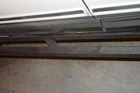 1993 Ford Bronco - Close-up of textured metal rock sliders mounted below the side trim of a white vehicle.