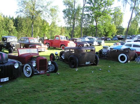 1978 Ford Bronco - A collection of custom hot rod vehicles are displayed on a sunny day in a park-like setting.