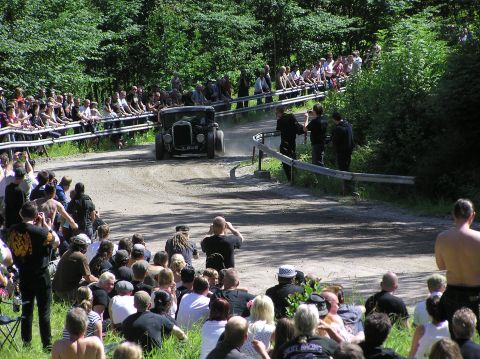 1978 Ford Bronco - A crowd watches a vintage car compete on a dusty track surrounded by trees.