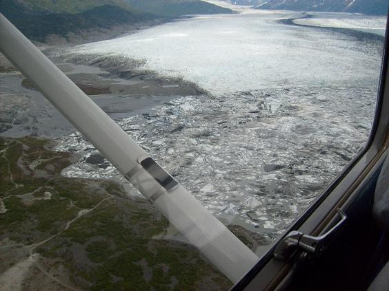 View from airplane window of a glacier and icy water, with a wing strut in the foreground