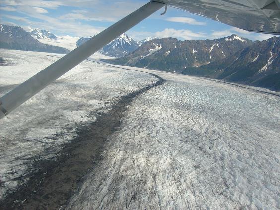 Aerial view of a vast glacier with snow-capped mountains in the background, seen from an airplane