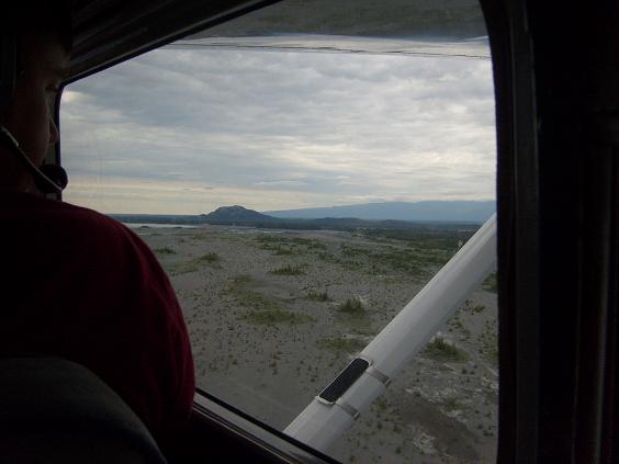 View from aircraft interior of a person in a red shirt looking out window at barren landscape and mountains