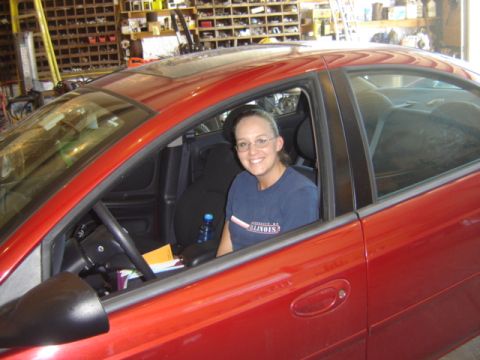 1992 Ford Bronco - A woman sits in the driver's seat of a red car, with shelves of parts visible in the background.