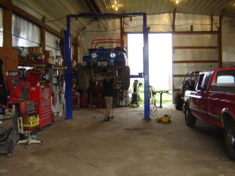 1992 Ford Bronco - A blue Jeep is elevated on a car lift inside a workshop, with a red pickup truck visible to the right.