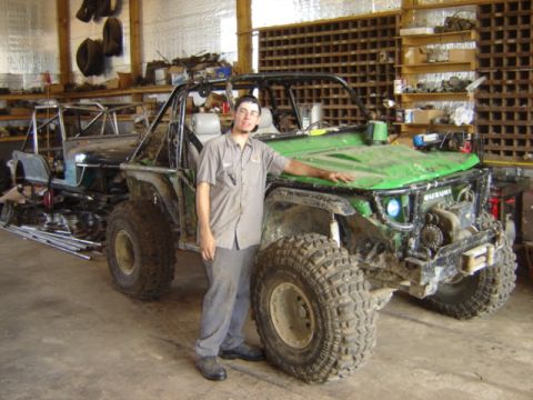 1992 Ford Bronco - A man stands beside a modified Suzuki Samurai in a workshop, with another vehicle project visible behind it.