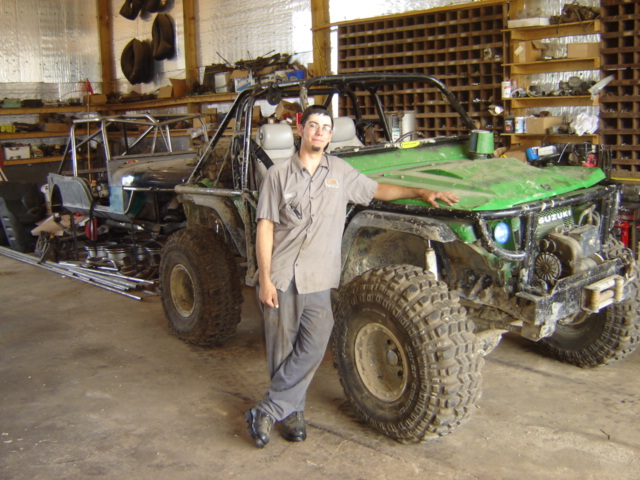 Green modified off-road vehicle with large tires and a roll cage, a man stands beside it