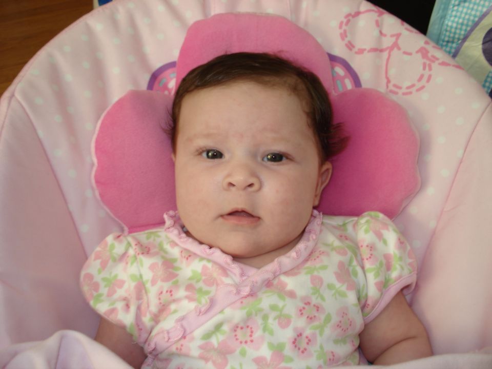Baby girl in a pink floral onesie lies in a pink baby bouncer