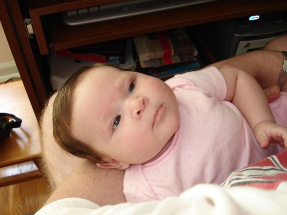 Baby lying on a person's lap, wearing a pink onesie