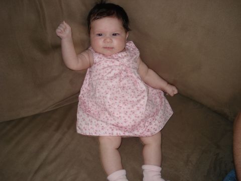 2000 Ford Crown Victoria - A baby girl wearing a pink floral dress and socks lies on a brown couch, looking towards the camera.