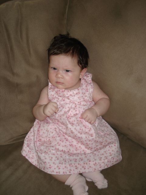 2000 Ford Crown Victoria - Baby girl in a pink floral dress and socks sits on a brown couch.