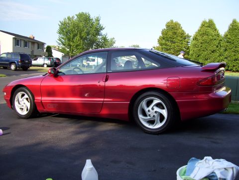 1995 Ford Probe - A red coupe is parked on an asphalt surface with other vehicles visible in the background.