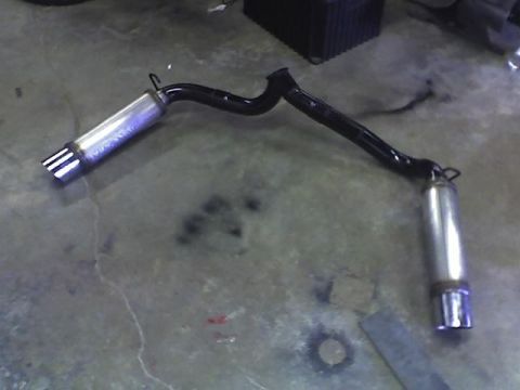 1988 Pontiac Fiero - Dual mufflers with quad-tip outlets are shown as a vehicle part on a concrete surface.