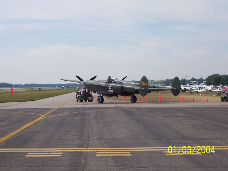 Lockheed P-38 Lightning airplane on tarmac with a tow vehicle attached
