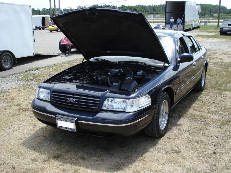 Dark blue 2000 Ford Crown Victoria with hood up, showing the engine bay. Parked outdoors on a dirt lot
