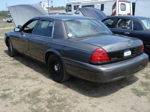 2000 Ford Crown Victoria - Two Ford Crown Victorias are parked outside, one with its hood open.