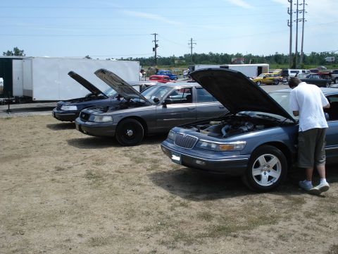 2000 Ford Crown Victoria - Three sedans, likely Ford Crown Victorias and a Mercury Grand Marquis, are parked with their hoods open.
