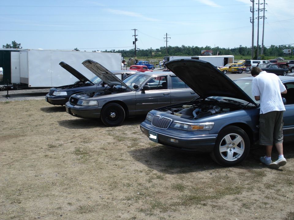 Three sedans with hoods open parked on gravel. Two Ford Crown Victorias and one Mercury Grand Marquis