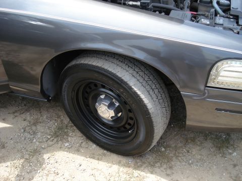 2000 Ford Crown Victoria - Close-up of the front passenger side of a dark gray Ford Crown Victoria, showing the wheel well and open hood.