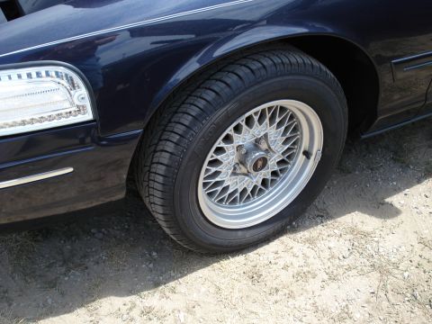 2000 Ford Crown Victoria - Close-up of a dark blue sedan's front wheel and fender, showing the tire and a chrome-accented body line.