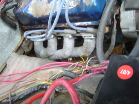 1979 Ford Bronco - Engine bay close-up of a blue Ford V8 valve cover with gray spark plug wires running down through separators to plugs in the head, above a…