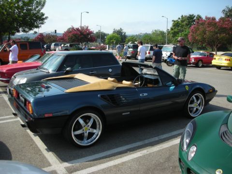 1998 Ford Crown Victoria - A dark blue convertible sports car is parked in a lot with several other vehicles and people visible.