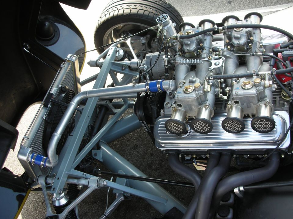 Close-up of a V8 engine with four dual-throat carburetors, chrome valve covers, and black exhaust headers