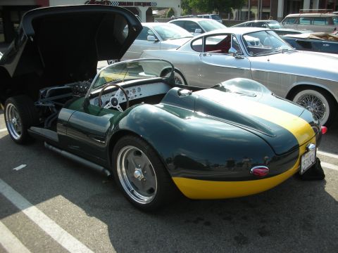 1998 Ford Crown Victoria - A dark green and yellow two-tone sports car is parked with its hood open, revealing the engine and interior. Other vehicles are visible in…