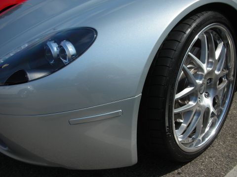 1998 Ford Crown Victoria - A close-up view of the front corner of a silver sports car, highlighting its custom alloy wheel and headlight assembly.