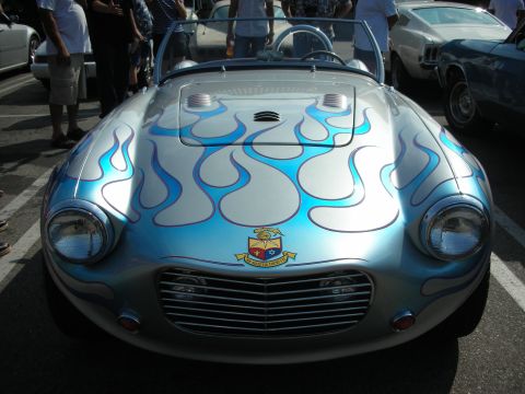 1998 Ford Crown Victoria - A custom hot rod with a unique flame paint job and a crest on the front is parked among other vehicles.