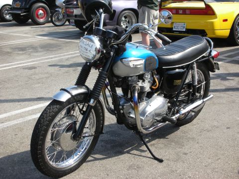 1998 Ford Crown Victoria - A Triumph Tiger 650 motorcycle is parked in a lot with other vehicles, displaying a "FOR SALE" sign on its headlight.