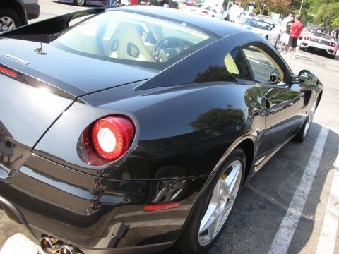 1998 Ford Crown Victoria - A black Ferrari coupe is parked in a lot, with other vehicles and people visible in the background.