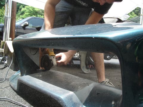 1995 Mazda MX-6 - A person uses an angle grinder on a teal car bumper. Another vehicle is parked behind.