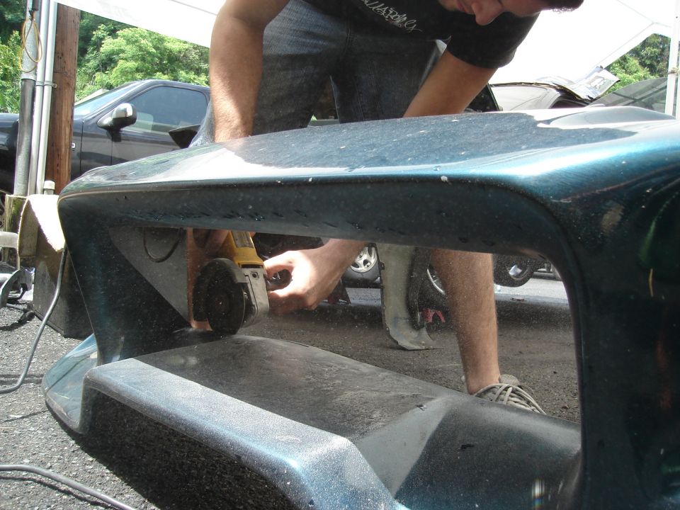 Teal car bumper being cut with an angle grinder. Another car is visible in the background