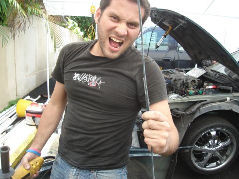 1995 Mazda MX-6 - Man works on a green car's engine bay, revealing chrome wheels and exposed mechanics.