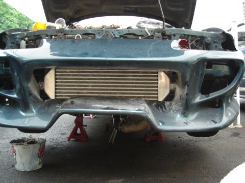 1995 Mazda MX-6 - The front of a car is elevated on jack stands, revealing an aftermarket intercooler mounted behind the bumper.