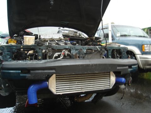 1995 Mazda MX-6 - Car engine bay with intercooler and blue hoses. Another vehicle is visible in the background.