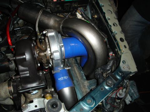1995 Mazda MX-6 - Custom turbocharger installation with blue silicone piping and metal exhaust components visible.