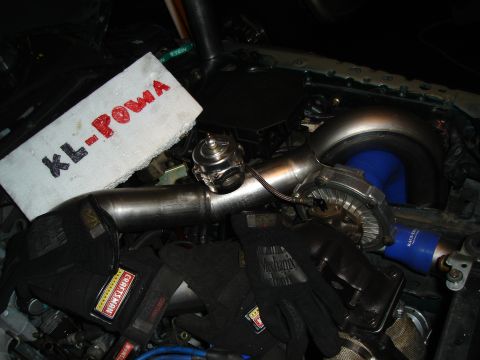 1995 Mazda MX-6 - Close-up view of engine components, including a turbocharger and blow-off valve, with work gloves nearby.