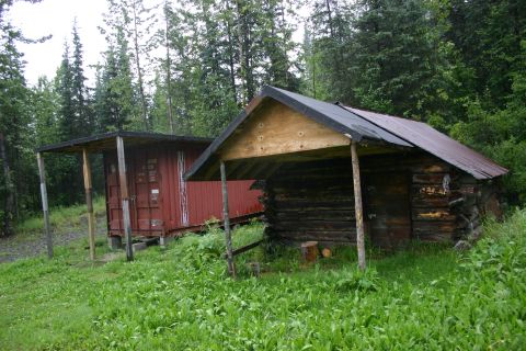 2003 Jeep TJ - A red shipping container and a log cabin sit side-by-side in a grassy, wooded area.