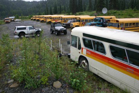 2003 Jeep TJ - A collection of buses and off-road vehicles are parked in an outdoor lot, with trees in the background.