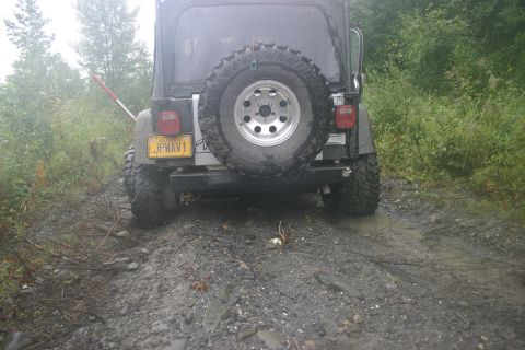 2003 Jeep TJ - This 2003 Jeep TJ is seen from the rear on a wet, muddy trail surrounded by foliage.