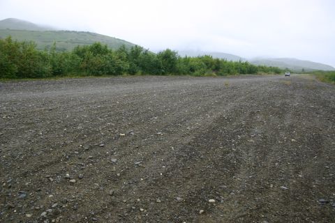 2003 Jeep TJ - A white SUV drives away on a gravel road with trees and hills in the background.