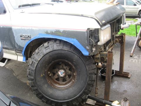 1990 Ford F-250 - Front fender and wheel of a 1990 Ford F-250 undergoing repairs, with blue tape around the wheel well.