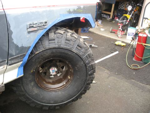1990 Ford F-250 - Close-up of a Ford F-250 Lariat fender and tire, with garage items in the background.