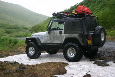 2003 Jeep TJ - A silver 2003 Jeep TJ Rubicon is parked on a snowy, muddy road with a roof rack carrying gear and a red gas can.