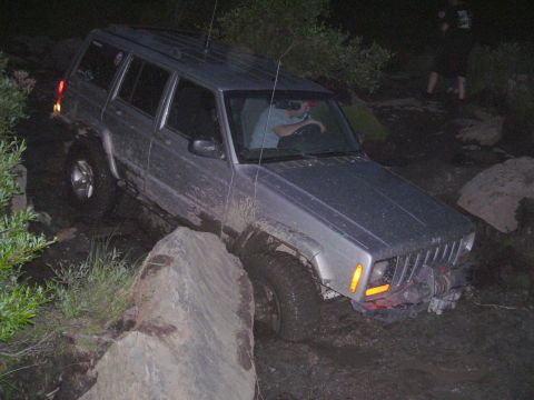 2003 Jeep TJ - A silver Jeep Cherokee XJ is shown off-roading over rocks and mud.