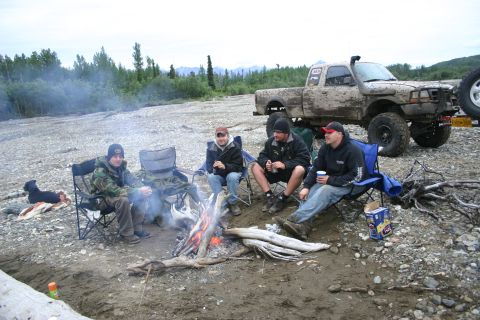 2003 Jeep TJ - A group of people relax around a campfire next to a heavily mud-splattered pickup truck.