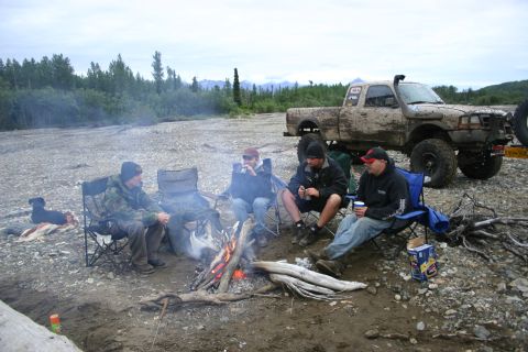 2003 Jeep TJ - A group of people camp around a fire with a muddy pickup truck parked nearby.