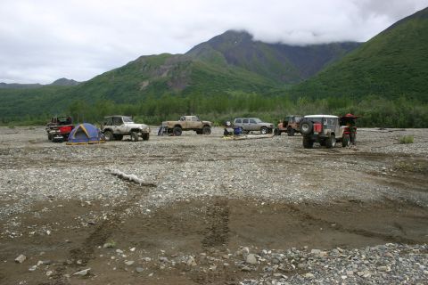 2003 Jeep TJ - Multiple off-road vehicles and camping gear are set up in a wide, rocky riverbed.