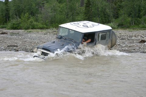 2003 Jeep TJ - A dark blue SUV with a white roof navigates through a shallow, muddy river.